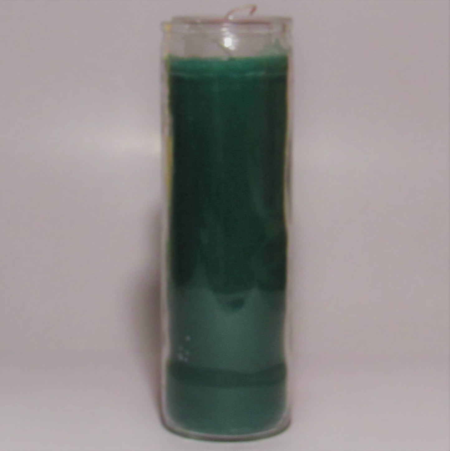 Green candle in a glass container on a light gray background